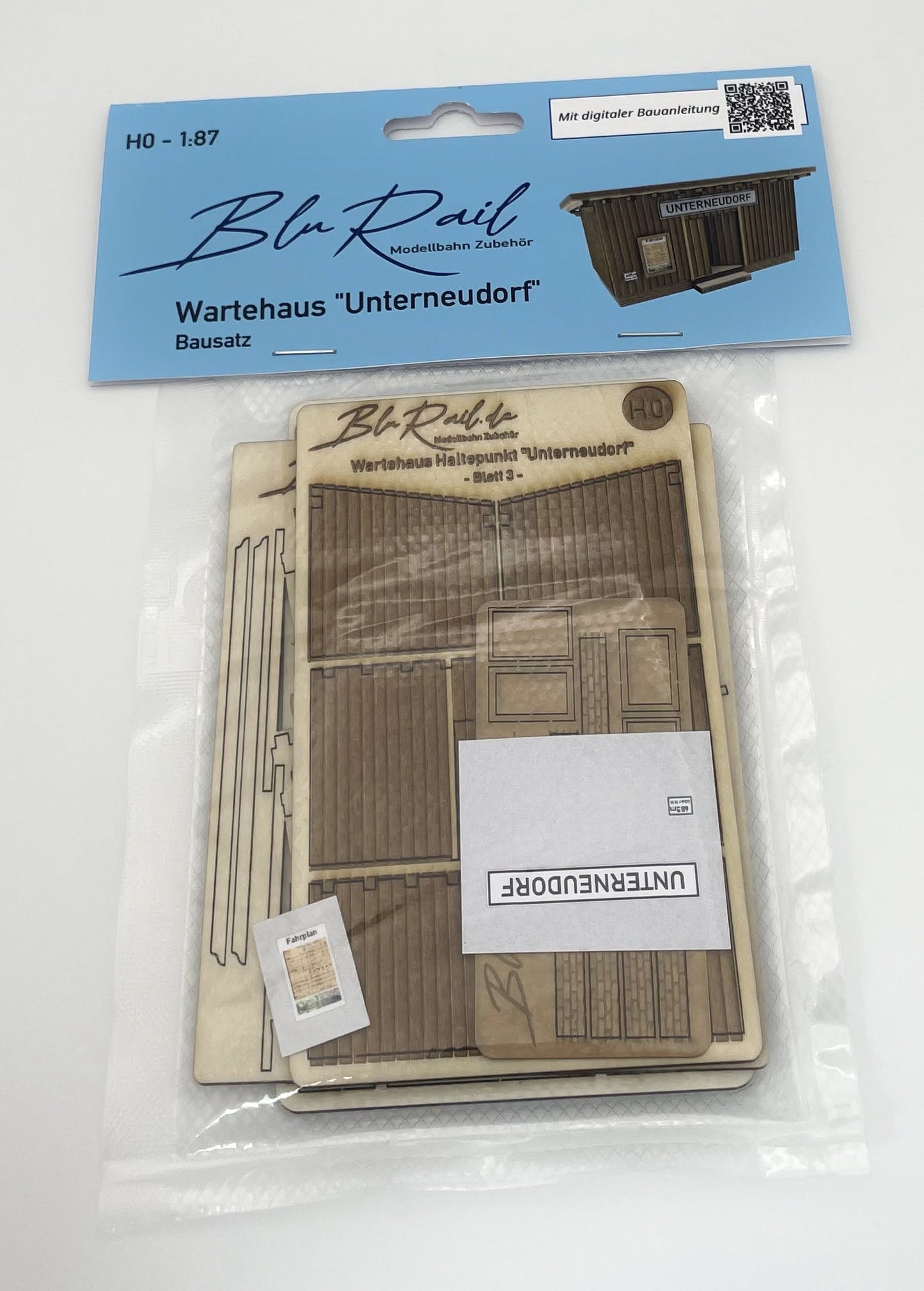 Beispielfoto eines Bausatzes des Wartehauses Haltepunkt "Unterneudorf" in Spur H0, hier in seiner Verpackung mit Folietüte und Produktlabel. Gezeigt wird die Vorderseite des verpackten Produktes.