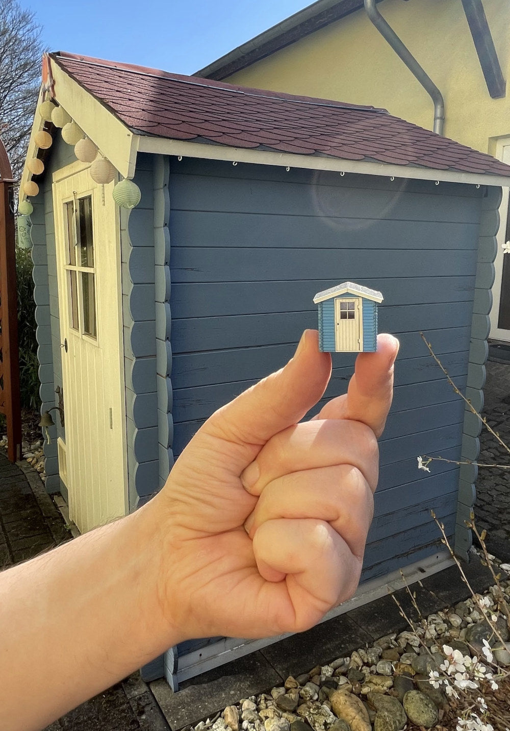Vorbild und Modell: die Kleine Gartenhütte H0 - 1/87 fertig montiert und im Hintergrund das Vorbild der Gartenhütte. Man sieht wie präzise mittels Lasercut gearbeitet werden kann und welch hohe Qualität der Bausatz bzw. das Endprodukt haben.